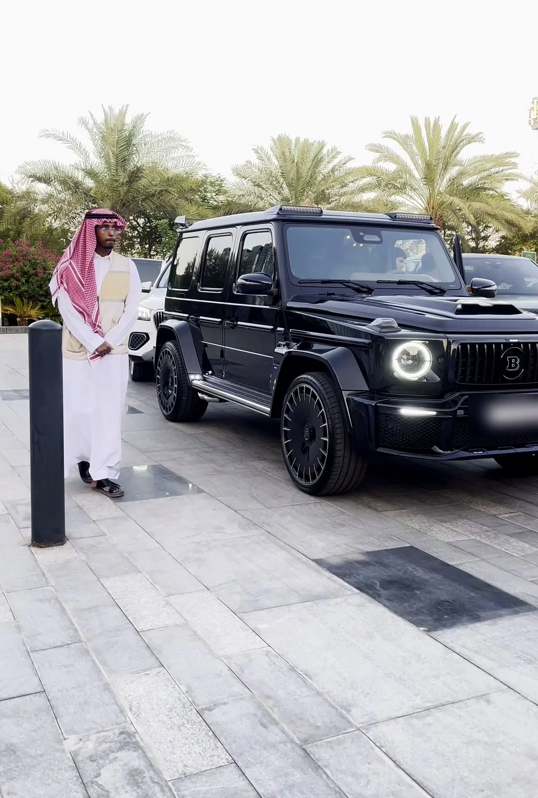 مستقبِل Valet بالزي السعودي بجانب سيارة فاخرة سوداء